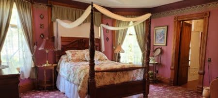Elegant guest room in a historic home with a four poster bed, red walls and patterned carpet