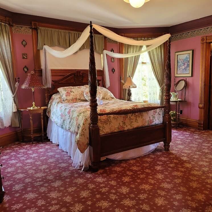 Elegant bedroom in reds and ivory with four poster bed, patterned carpet and large windows