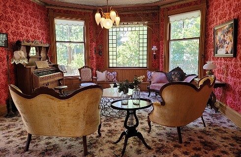 Sitting parlor with upholstered chairs and couch, organ and decorative red velvet wallpaper