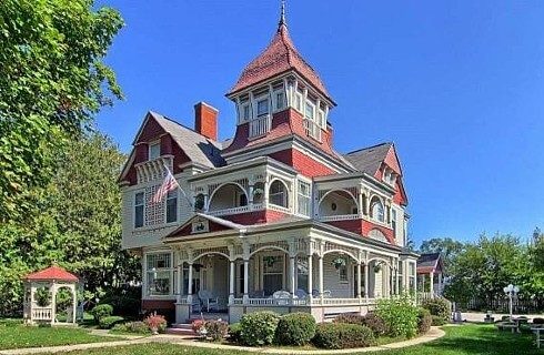 Outdoor view of a large red and white historic home with wrap around porch and surrounded by trees