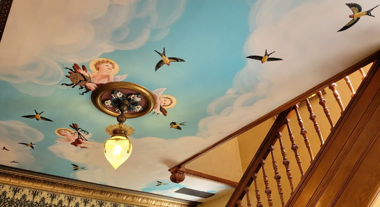 View of a ceiling featuring the painting of angles and birds among clouds and blue skies