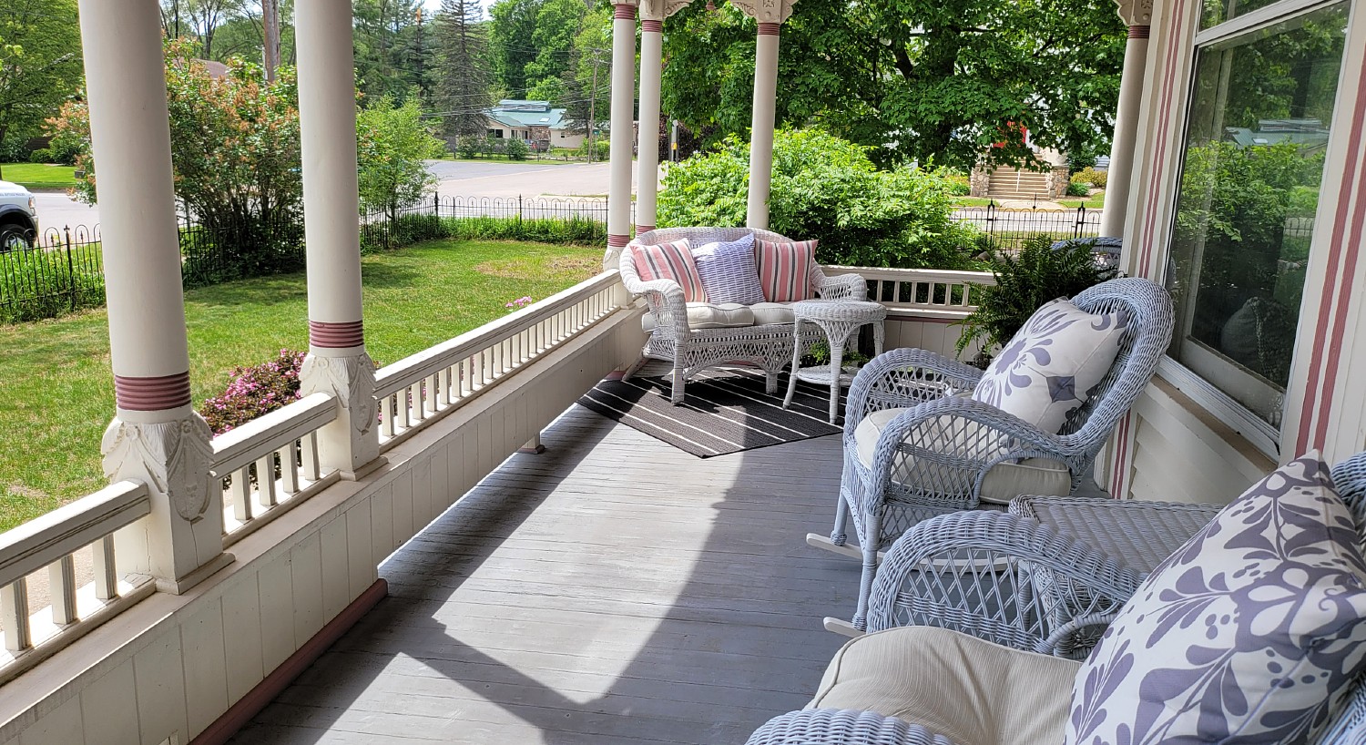 Spacious outside front porch with grey wicker furniture overlooking lawn and street