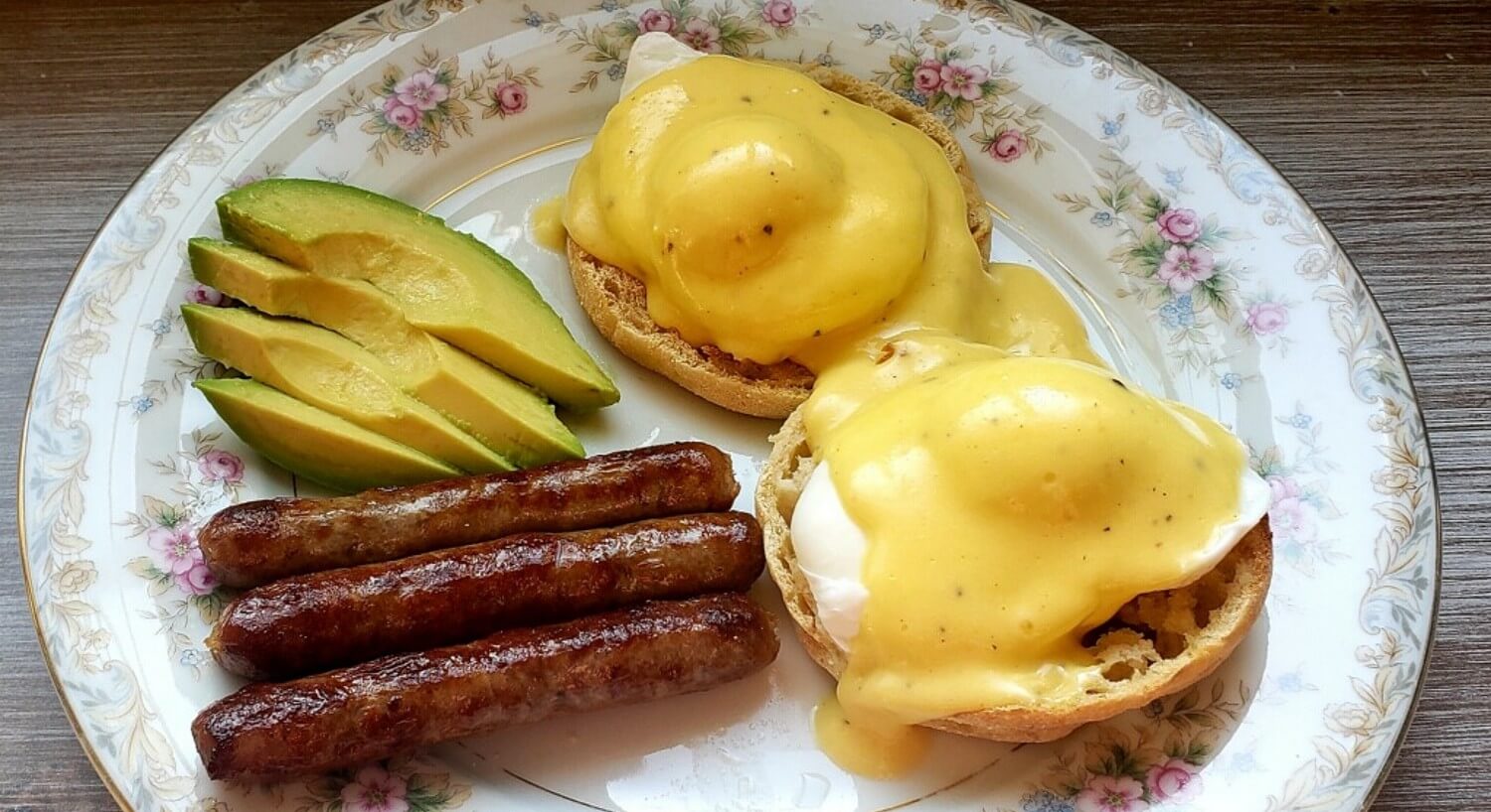 Floral china plate with eggs benedict, sausage links and avocado slices