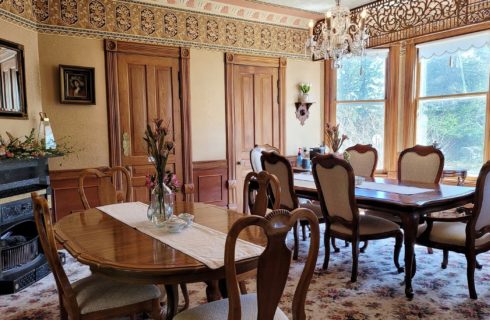 Large dining room in a historic home with two tables with chairs, fireplace and large bay window