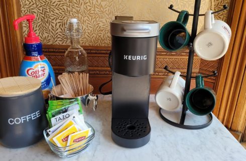 White marble table holding a coffee maker, rack of mugs and various items to make coffee