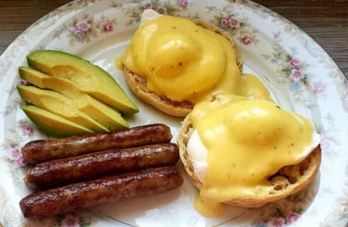Floral china plate with eggs benedict, sausage links and avocado slices