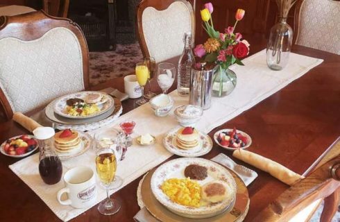 Beautiful antique dining table set for breakfast with a white runner and vase of flowers