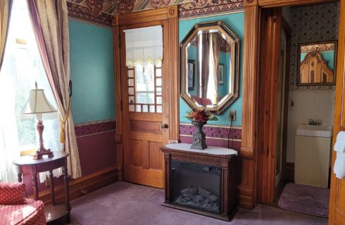 Corner of a bedroom with doorway into a bathroom, gas fireplace below large mirror