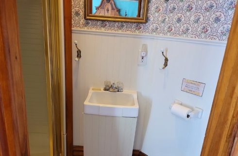 Small bathroom with single sink, stand up shower and white bead board with wallpapered wall above