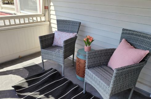 Outdoor patio with two grey wicker chairs with pink cushions and black and white striped rug