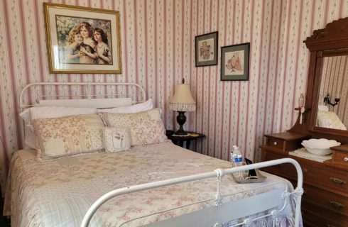 Bedroom with wrought iron bed, antique dresser with mirror and striped wallpaper