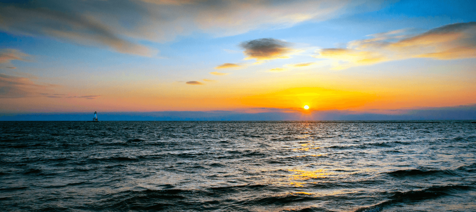 Large body of open water at sunset with a lighthouse in the distance