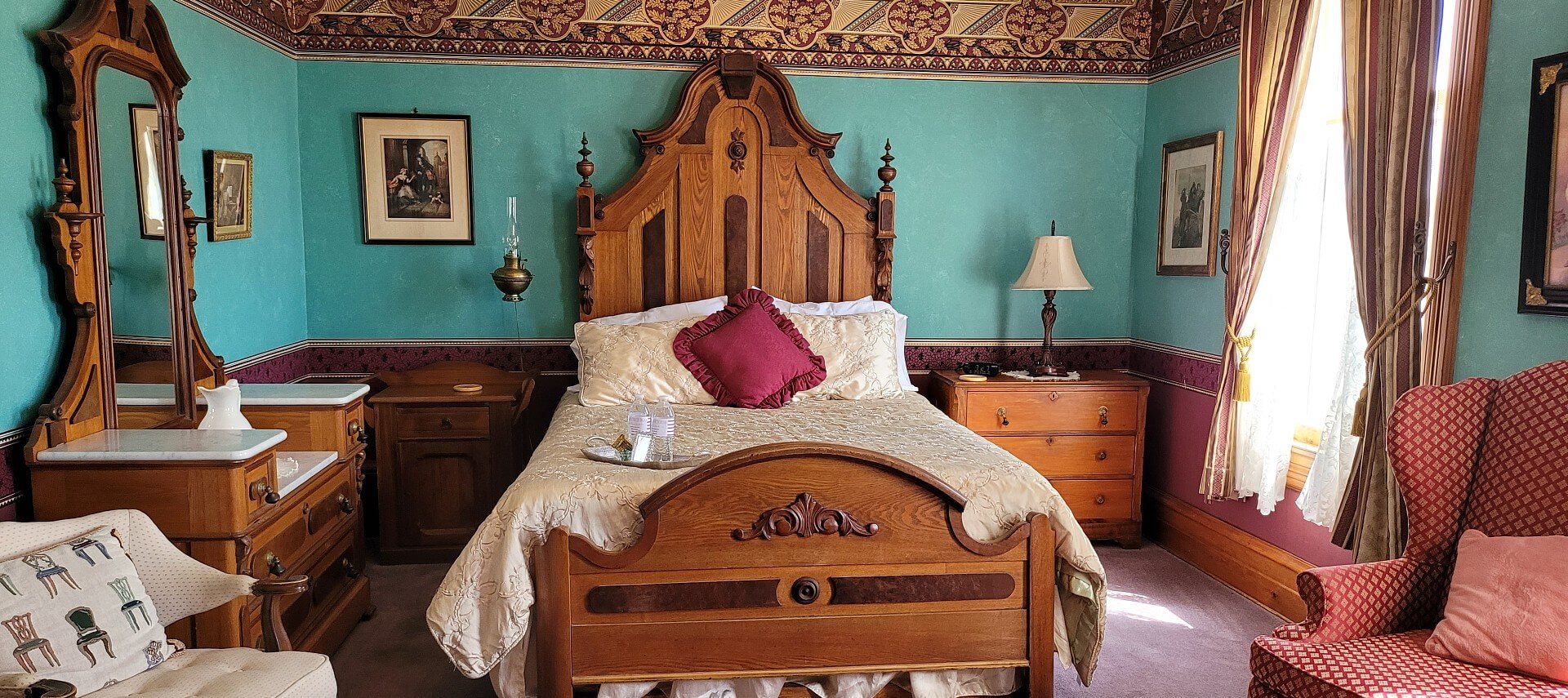 Elegant bedroom with antique bed, dresser with mirror, sitting chairs and bright window