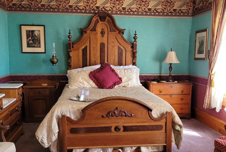 Elegant bedroom with antique bed, dresser with mirror, sitting chairs and bright window