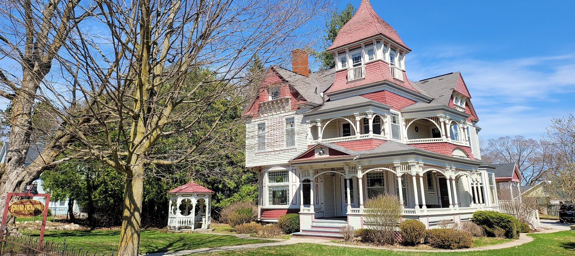 Outdoor view of a large red and white historic home with wrap around porch and small gazebo