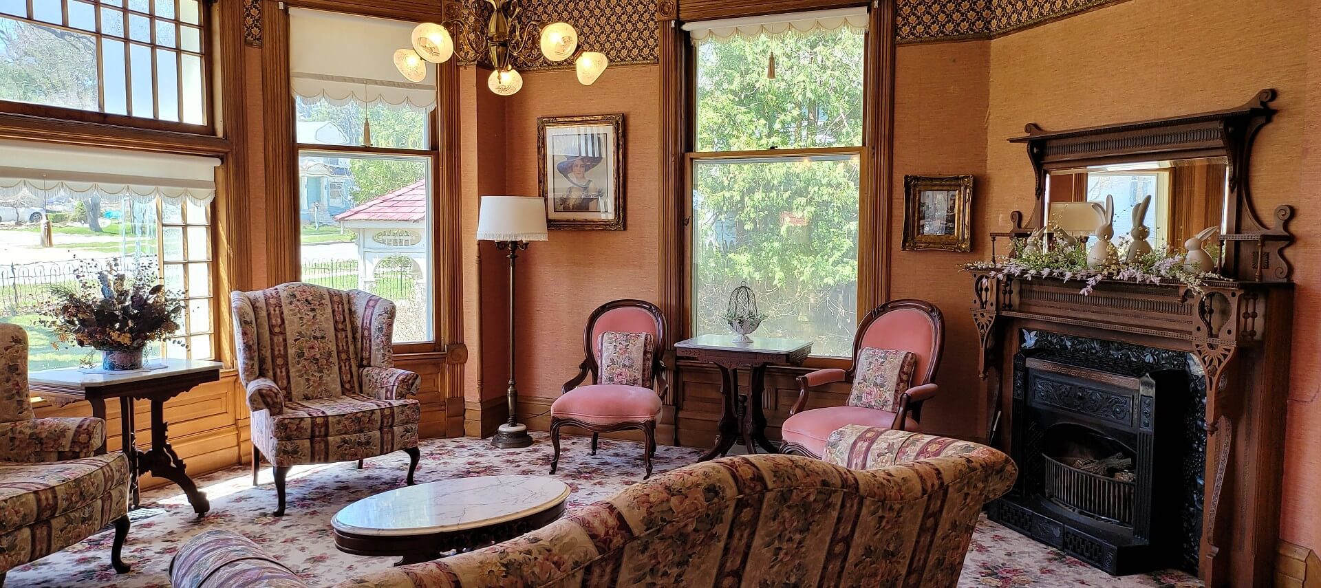 Bright sitting room of a historic home with couch, four chairs, fireplace and large windows