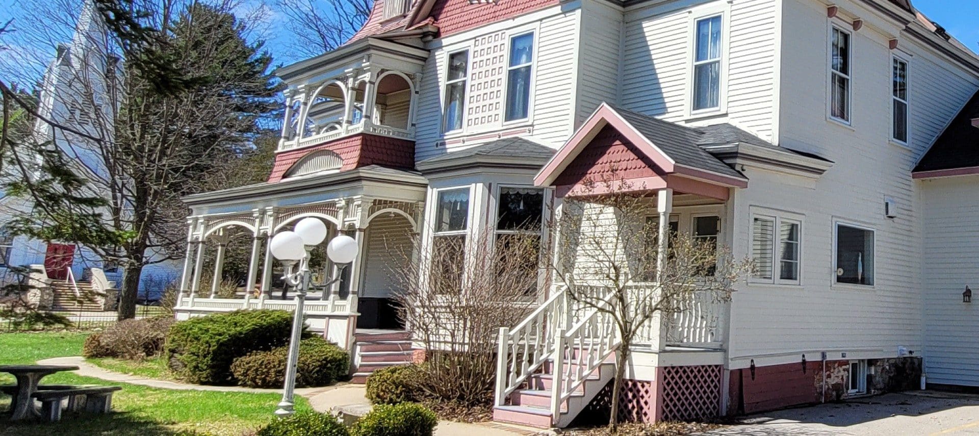 Side view of the outside of a large historic home with white siding and red accents