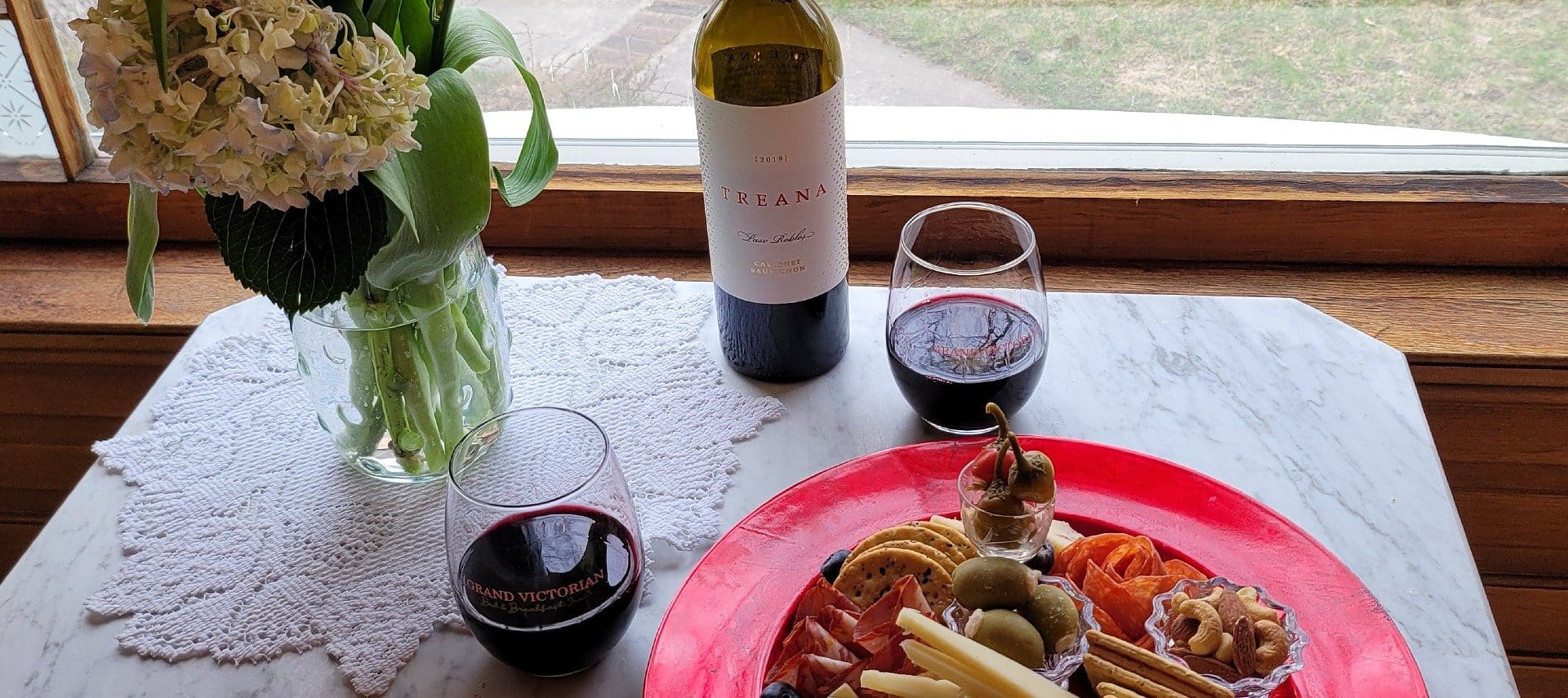 Small marble table holding a charcuterie plate, a bottle of wine and two glasses of red wine