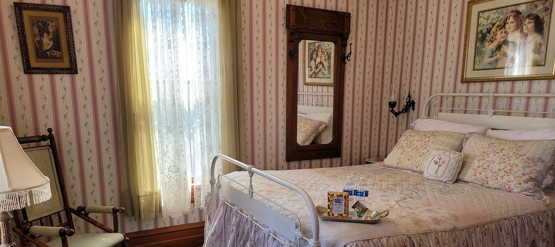 Elegant bedroom with wrought iron bed, sitting chair with lamp, large window and striped wallpaper