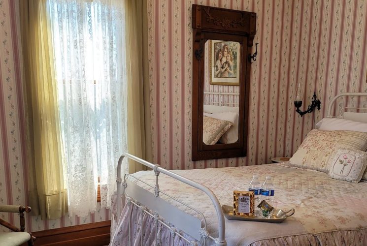 Elegant bedroom with wrought iron bed, sitting chair with lamp, large window and striped wallpaper