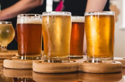 Five glasses on a wooden tray filled with different types of beer