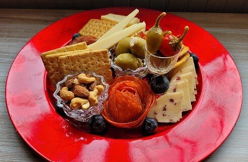 Red, circular charcuterie plate of cheeses, crackers, meats and olives