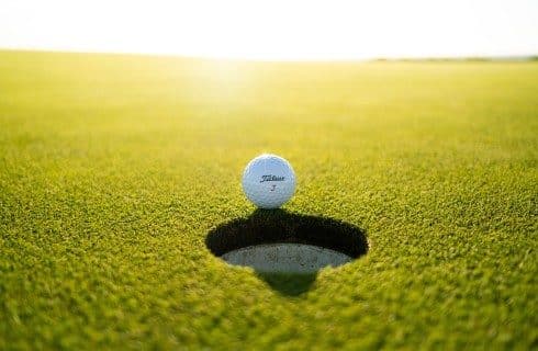 A single white golf ball at the edge of a hole on a golf green