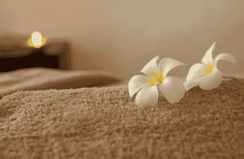 Table covered with a brown towel and white flowers with candle lit in background