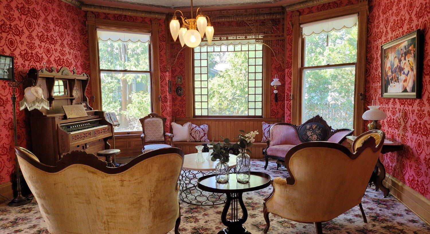 Sitting parlor with upholstered chairs and couch, organ and decorative red velvet wallpaper