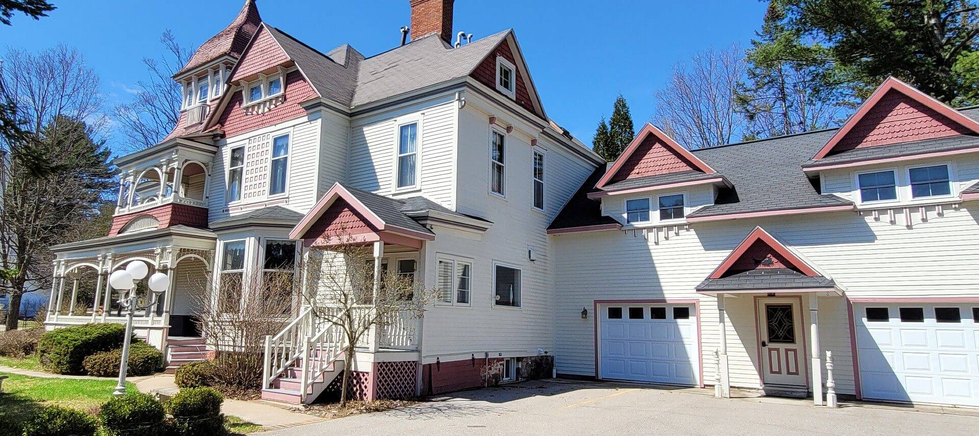 Side view of a large red and white historic home with wrap around porch and garage with two doors