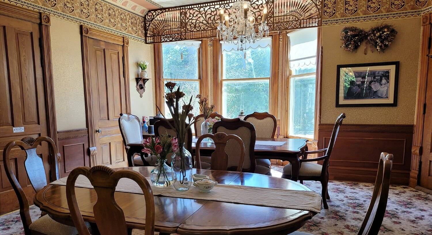 Dining room of a historic home with two tables, ten chairs and large bay window