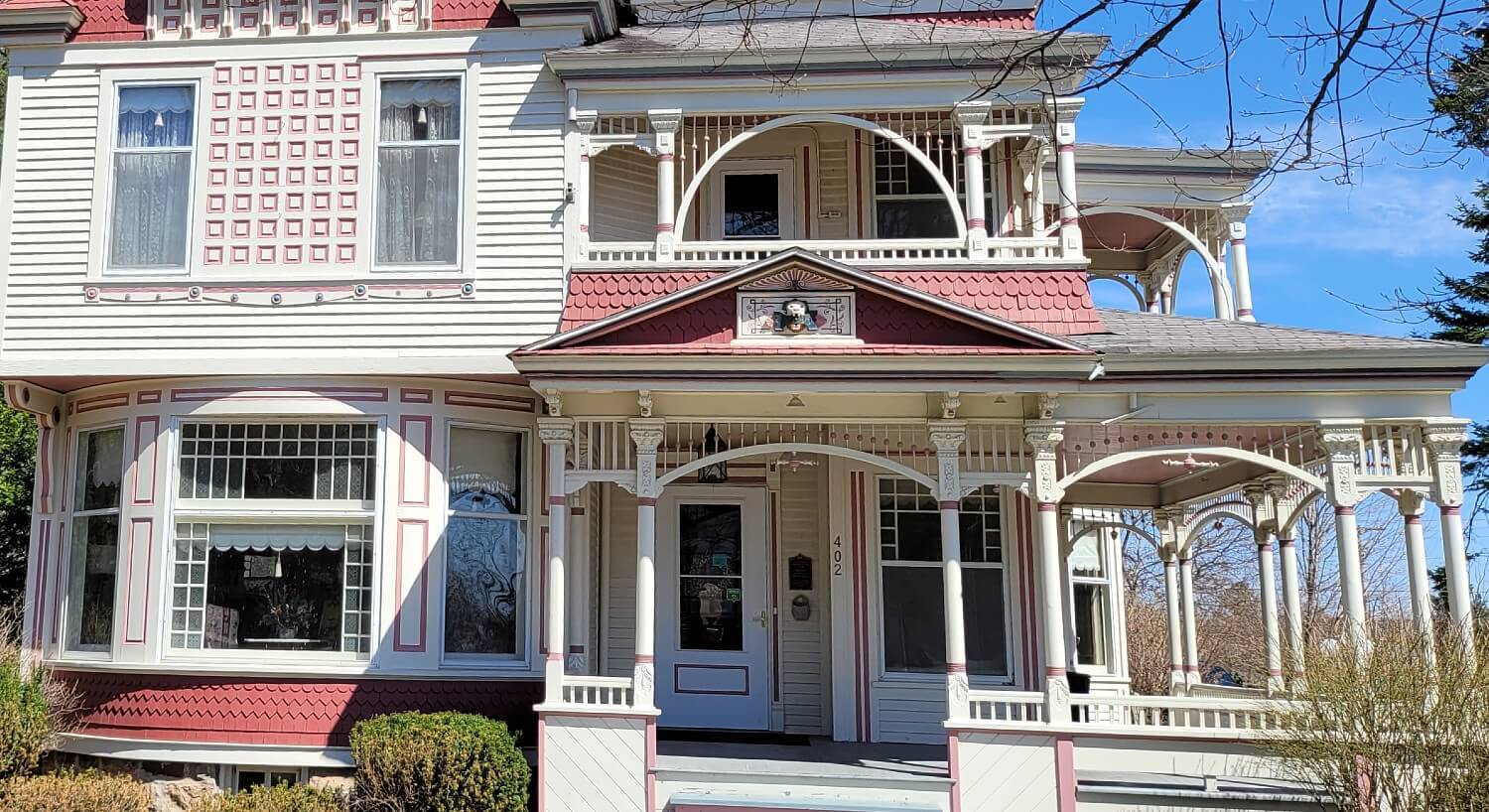 Front facade of a large historic home with white siding, red accents, and large wrap-around patio