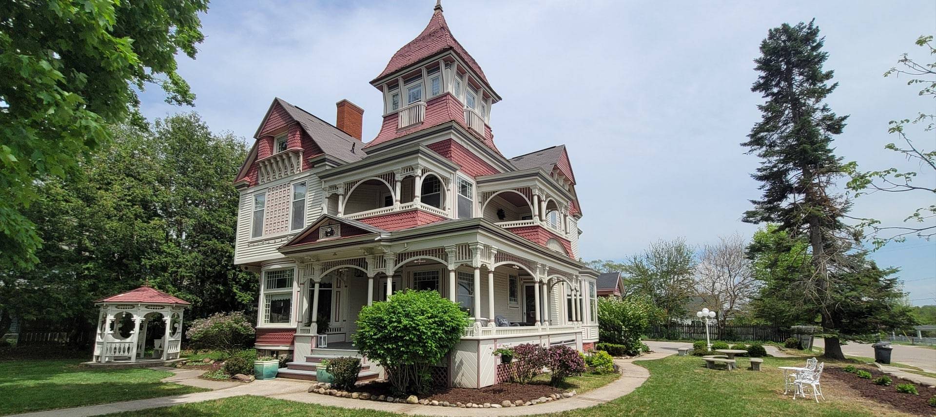 Outdoor view of a large red and white historic home with wrap around porch and small gazebo