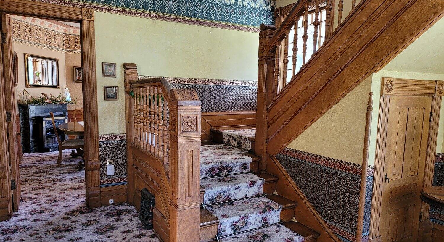 Front entry of a historic home showing a carpeted stairway and doorway leading into a dining room