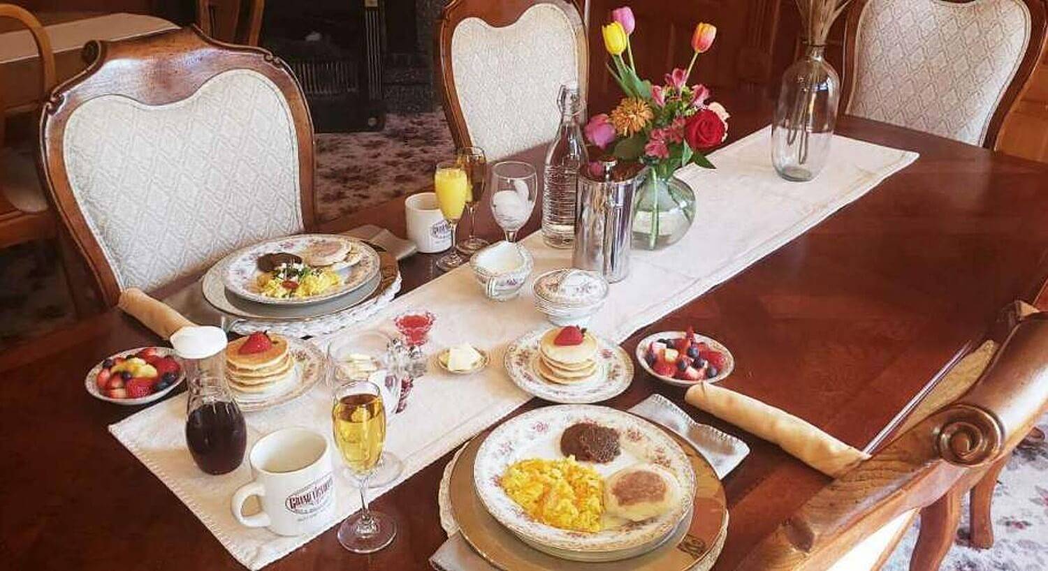 Beautiful antique dining table set for breakfast with a white runner and vase of flowers